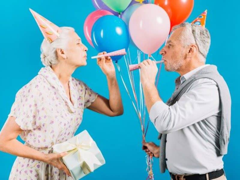 side-view-of-senior-couple-looking-at-each-other-blowing-party-horn-on-blue-backdrop_23-2147950917-1